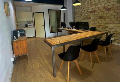 Communal area with a long timber coworking table, black chairs, and exposed brick walls.