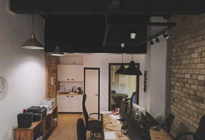 Open plan office area featuring long wooden desks and industrial black pendant lighting.