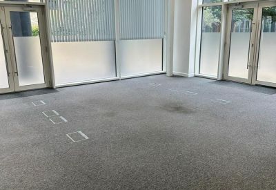 Bright, empty office space with large floor-to-ceiling windows and grey carpeting.