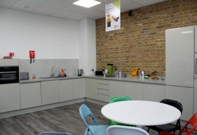 Modern communal kitchen area with white cabinetry and an exposed brick feature wall.