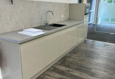 Modern office kitchenette with white cabinetry, wood-style flooring, and a grey countertop.