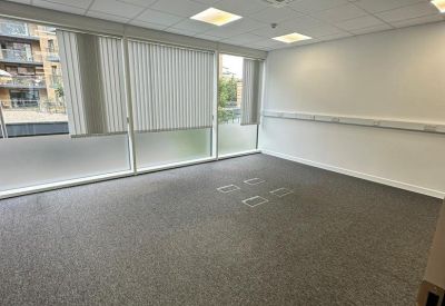 Bright, empty open-plan office space with grey carpeting and large windows with blinds.