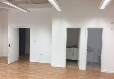 Empty office area showing an open doorway and a small kitchenette area visible in an adjacent room.