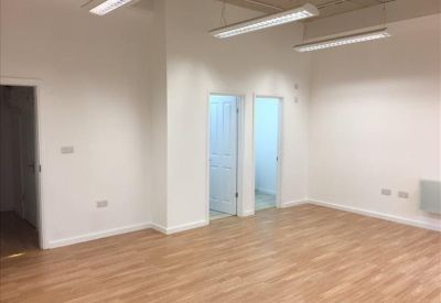 Bright, empty office space featuring light wood floors and white walls with two internal doorways.