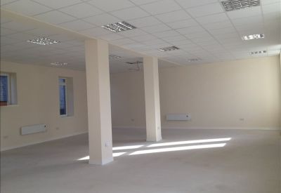 Bright open-plan office space with white walls, pillars, and suspended ceiling grid.