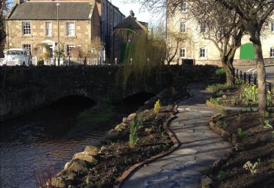 Stone-paved garden path winding alongside a stream and flower beds.