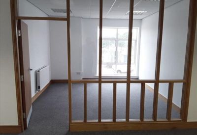 Private office space viewed through a wood-framed glass partition with a large window providing natural light.