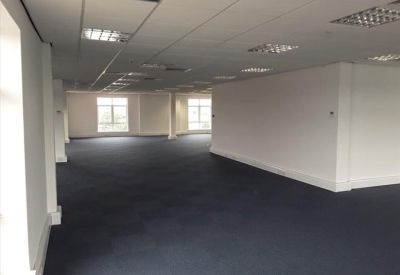 Large empty office floor with white walls, blue carpet, and bright windows at the far end.