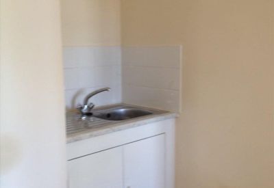 Compact kitchenette area with a stainless steel sink, white cabinetry, and tiled splashback.