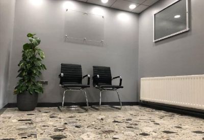 Reception waiting area with two black leather chairs, a potted plant, and stone-patterned floor.