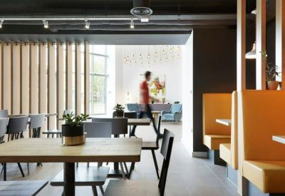Modern dining area with light wood tables, yellow booth seating, and slatted wood partitions.