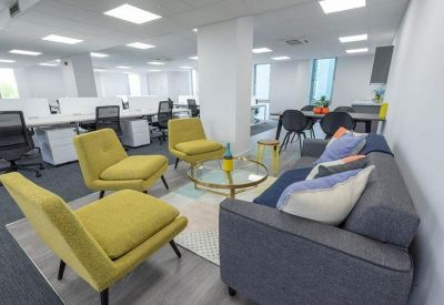 Modern open-plan office with grey sofas and yellow armchairs centered around a rug.