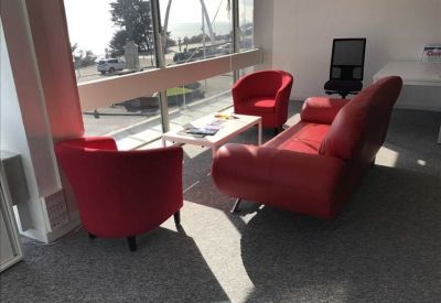 Bright lounge area with red armchairs, a matching sofa, and sea views through floor-to-ceiling windows.