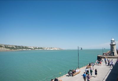 Coastal view from the pier featuring a white lighthouse and blue sea.