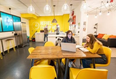 Spacious breakout area with a yellow feature wall and people working at a wooden communal table.