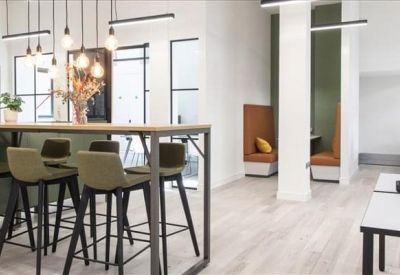 Communal breakout area with a high wooden table, olive green stools, and orange privacy booths.