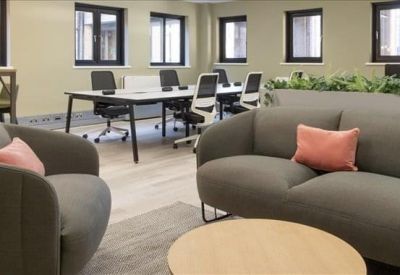 Modern lounge area with grey sofas, pink cushions, and a white coworking table in the background.