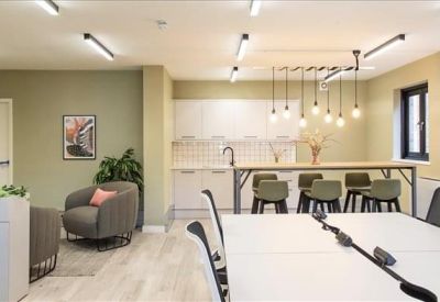 Bright breakroom featuring a white kitchenette, breakfast bar with stools, and comfortable armchairs.