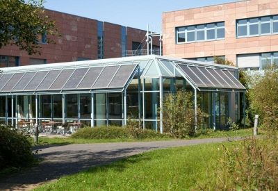 Glass-walled cafeteria or breakout area with solar panels on the roof and outdoor greenery.