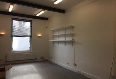 Bright private office suite with white walls, wall-mounted shelving, and dark ceiling beams.