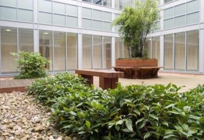 Outdoor communal courtyard with manicured plants, wooden benches, and large windows.