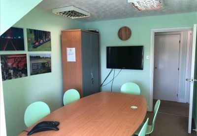 Meeting room with an oval wooden table, green chairs, and a wall-mounted television.