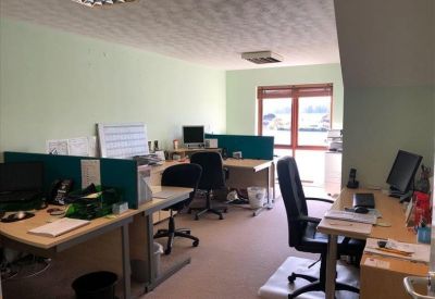 Open-plan office area with several desk pods and a view through a window.