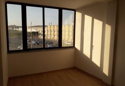 Bright corner office space with large windows overlooking an industrial area and parking lot.