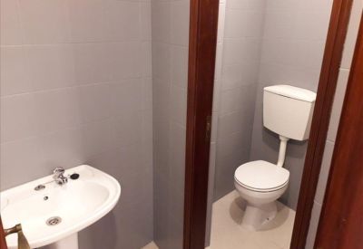 Small restroom area featuring a white pedestal sink and a separate toilet stall.