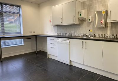 Modern office kitchen with white cabinetry, dark grey flooring, and integrated dishwasher.