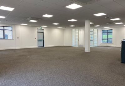 Large empty open-plan office with grey carpet and square ceiling lights.