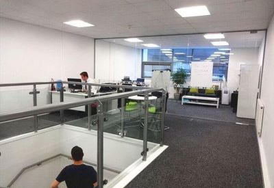 Glass-walled office space with workstations overlooking a mezzanine stairwell.