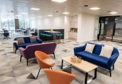 Modern lounge area with blue and purple sofas, orange armchairs, and a stylish patterned carpet.
