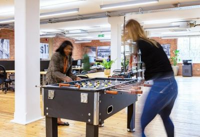 Staff playing foosball in a bright, modern breakout area with wooden floors.
