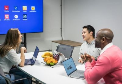 Collaborative meeting space with a large digital screen and people using laptops.