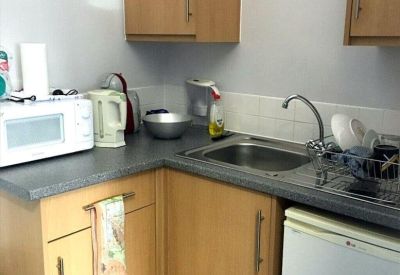 Small office kitchen with wood-finish cabinets, a microwave, kettle, and sink.