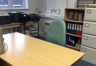 Private office featuring a large wooden desk, green swivel chair, and shelving units.