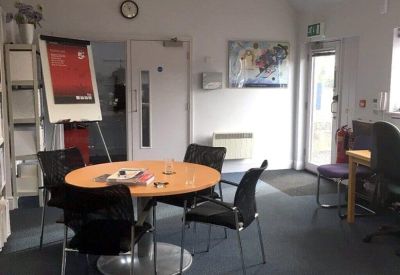 Bright meeting room with a round wooden table, black chairs, and a whiteboard.