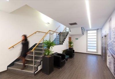 Modern lobby area featuring a sleek staircase with glass balustrades, black armchairs, and indoor plants.