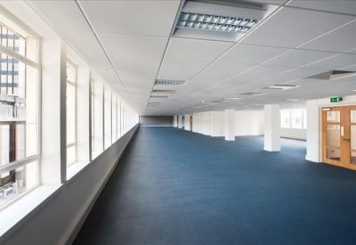 Spacious, open-plan office floor with blue carpeting and long rows of windows providing natural light.