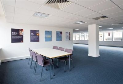 Simple meeting area with a white table, purple chairs, and information posters on the wall.