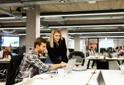 Two colleagues collaborating at a white desk in a bright, modern open-plan office.
