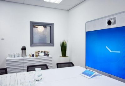 Bright meeting room with a large video conferencing screen and white boardroom table.
