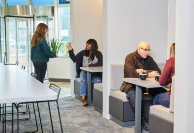 Modern breakout area featuring grey booth seating and white tables where people are working.