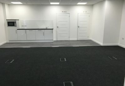 Communal kitchen area with white cabinetry, integrated microwave, and dark grey carpeting.