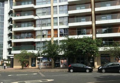 Ground floor exterior facade featuring glass-fronted commercial units and street-side trees.