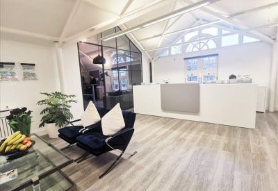 Modern white reception area with velvet armchairs, glass coffee table, and exposed roof beams.