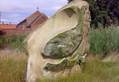 Large abstract stone sculpture situated in a grassy field near the brick buildings.
