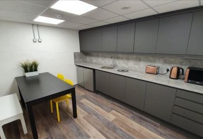 Modern communal kitchen and dining area with grey cabinetry and wooden floors.