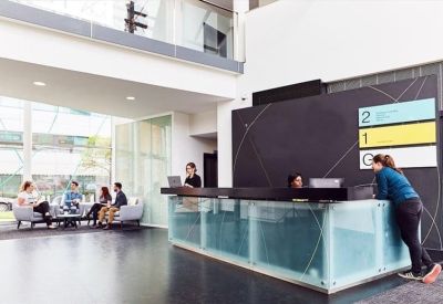 Modern glass-fronted reception desk with seating area and floor directory signage.